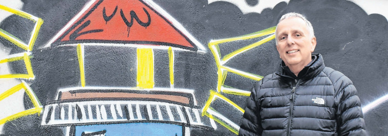 Jürgen Rotter vor Graffitiwand, die einen Leuchtturm zeigt