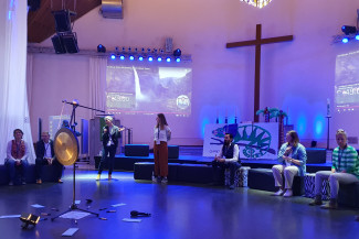 Blauerleuchteter Lux-Kirchenraum mit Menschen auf Sitzhockern