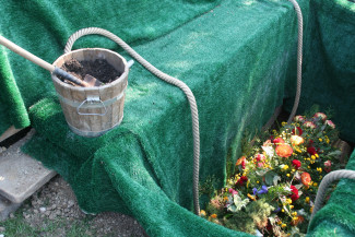 Offenes Grab mit Eimer und Blumengebinde