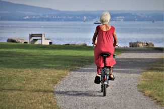 Frau in rotem Kleid auf Fahrrad Richtung See unterwegs