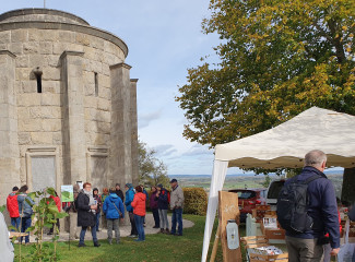 Menschen vor Kriegerdenkmal im Hintergrund, rechts Pavillon und Baum