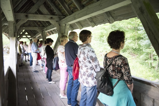 Menschen auf einer überdachten Tauberbrücke mit Blick in das Grün