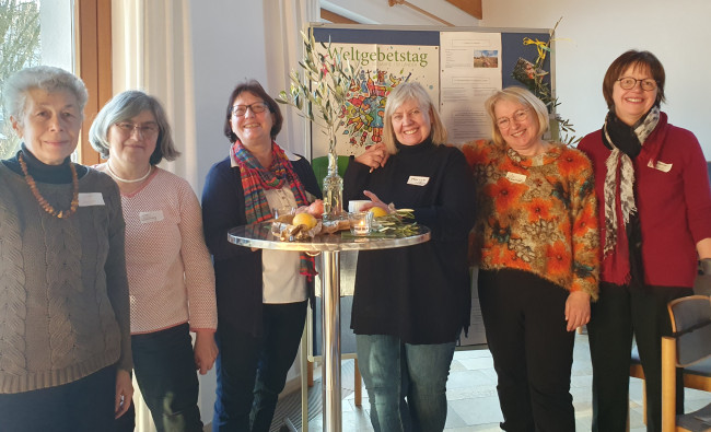 Gruppenbild mit sechs Frauen, die sich freuen, vor Plakat Weltgebetstag 2024