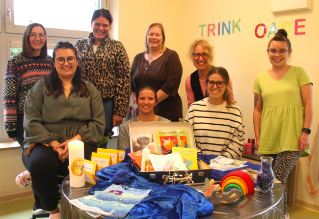 Erzieherinnen um einen Tisch herum mit Taufkoffer drauf